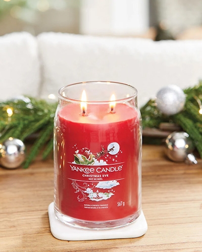 Bougie Yankee Candle Christmas Eve allumée avec décorations de Noël en arrière-plan.